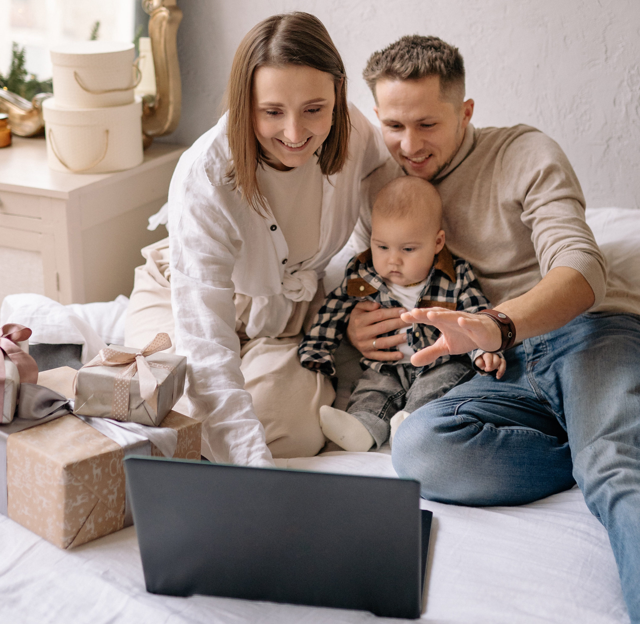 Happy mother, father, and baby opening gifts and facetiming family. Happy about their investments and future.